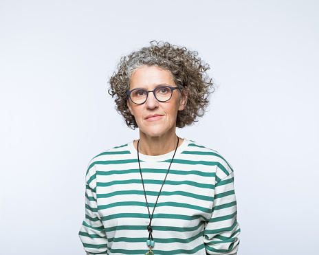 Portrait of mature woman wearing striped blouse and eyeglasses, looking at camera. Studio shot, grey background.