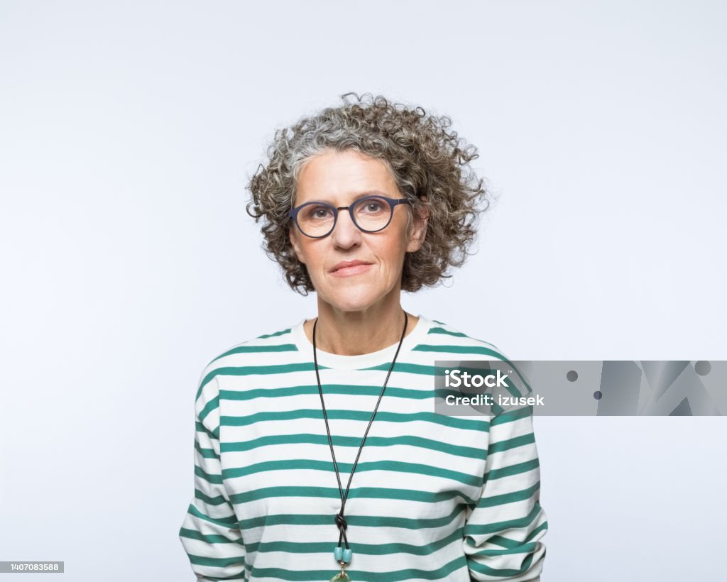 Portrait of confident mature women Portrait of mature woman wearing striped blouse and eyeglasses, looking at camera. Studio shot, grey background. Serious Stock Photo