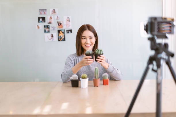 istock Beautiful Asian woman vlogger influencer work on home studio record video camera selfie shoot filming for live sell and show cactus, plants to channel. Happy Blogger, freelance work online marketing. 1407084183