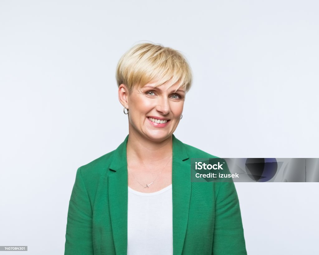 Portrait of happy businesswoman Portrait of confident mature woman wearing green jacket, smiling at camera. Studio shot, grey background. Blond Hair Stock Photo