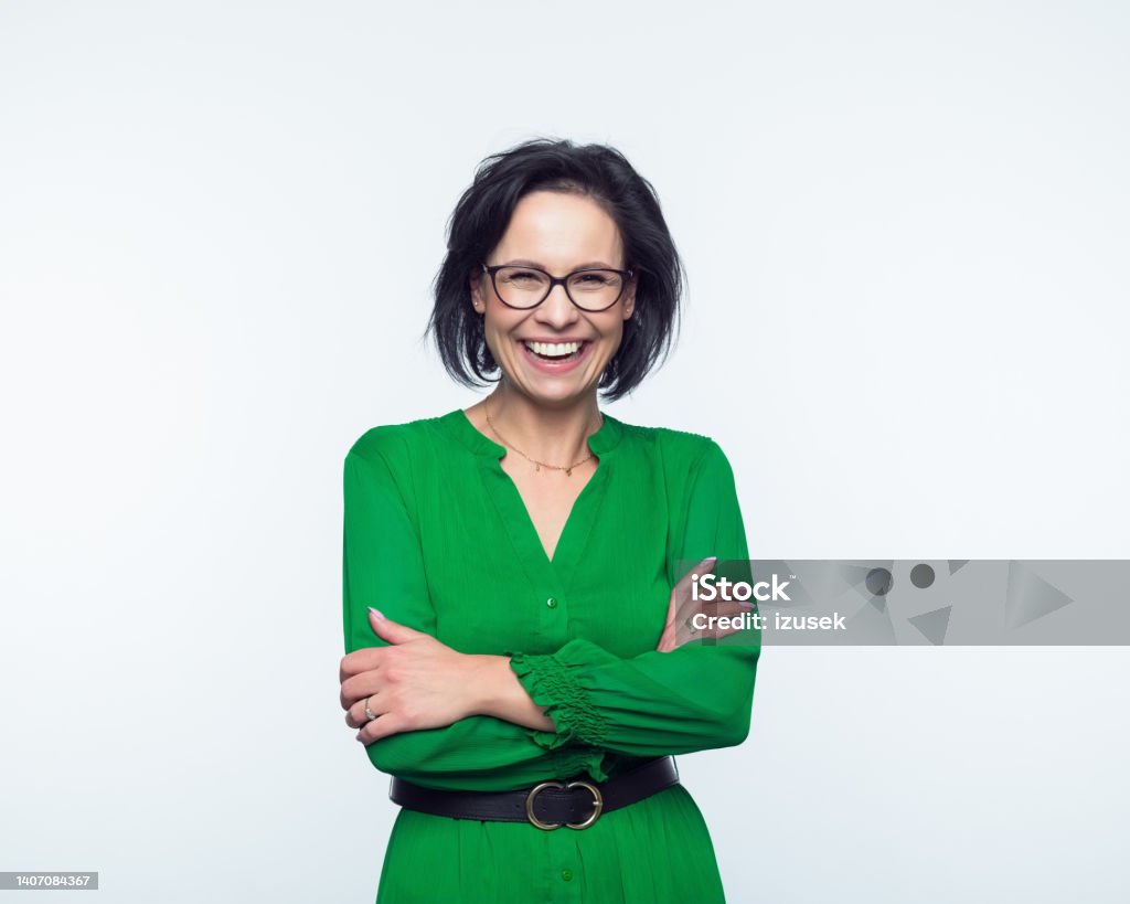 Portrait of happy mature women Portrait of confident mature woman wearing green dress, standing with arms crossed and smiling at camera. Studio shot, grey background. Business Stock Photo