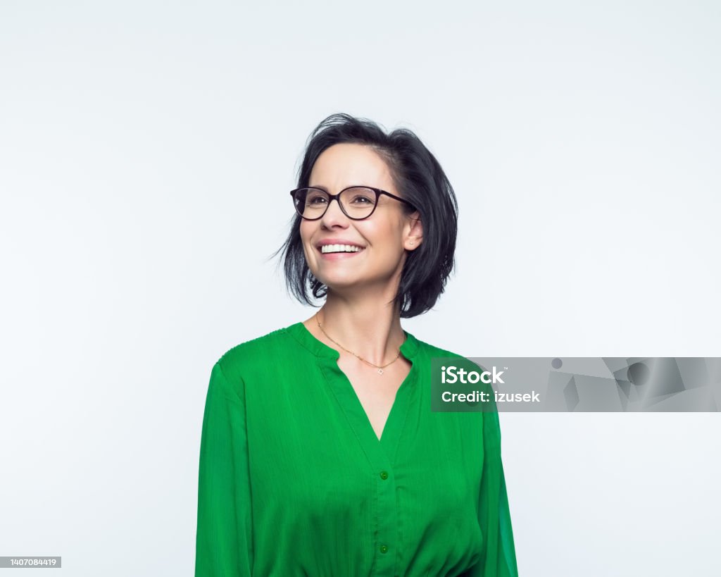 Portrait of happy mature women Portrait of confident mature woman wearing green dress, looking away and smiling. Studio shot, grey background. Women Stock Photo