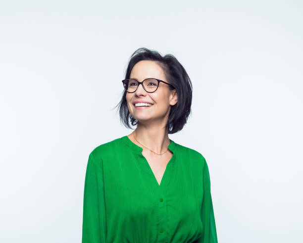 Portrait of happy mature women Portrait of confident mature woman wearing green dress, looking away and smiling. Studio shot, grey background. brown haired person stock pictures, royalty-free photos & images