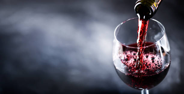 Pouring glass of red wine from a bottle in wide banner shape or copy space for text.. stock photo