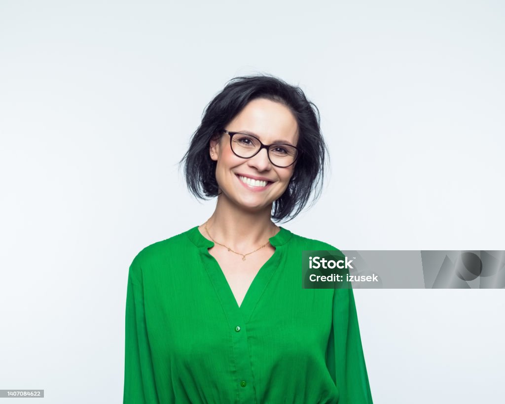 Portrait of smiling mature women Portrait of confident mature woman wearing green dress, smiling at camera. Studio shot, grey background. Businesswoman Stock Photo