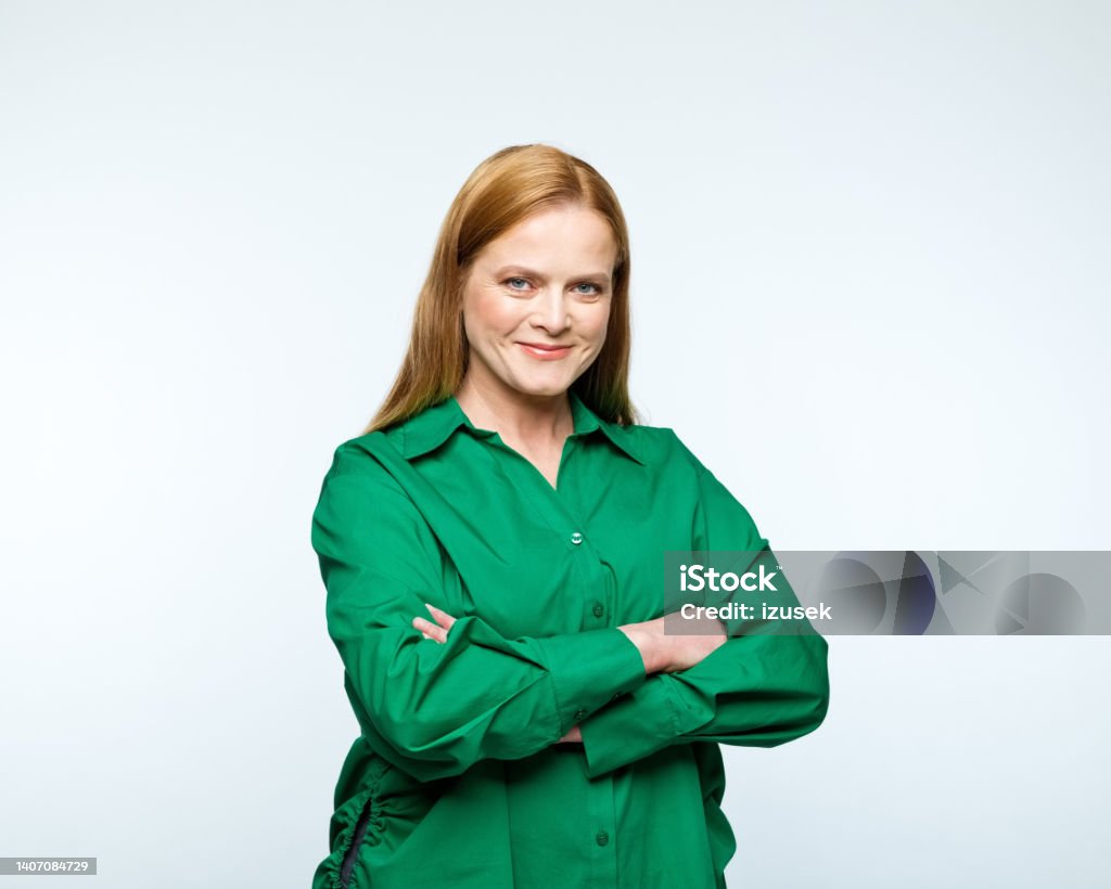 Portrait of smiling mature women Portrait of confident mature woman wearing green shirt, standing with arm crossed and smiling at camera. Studio shot, grey background. Entrepreneur Stock Photo