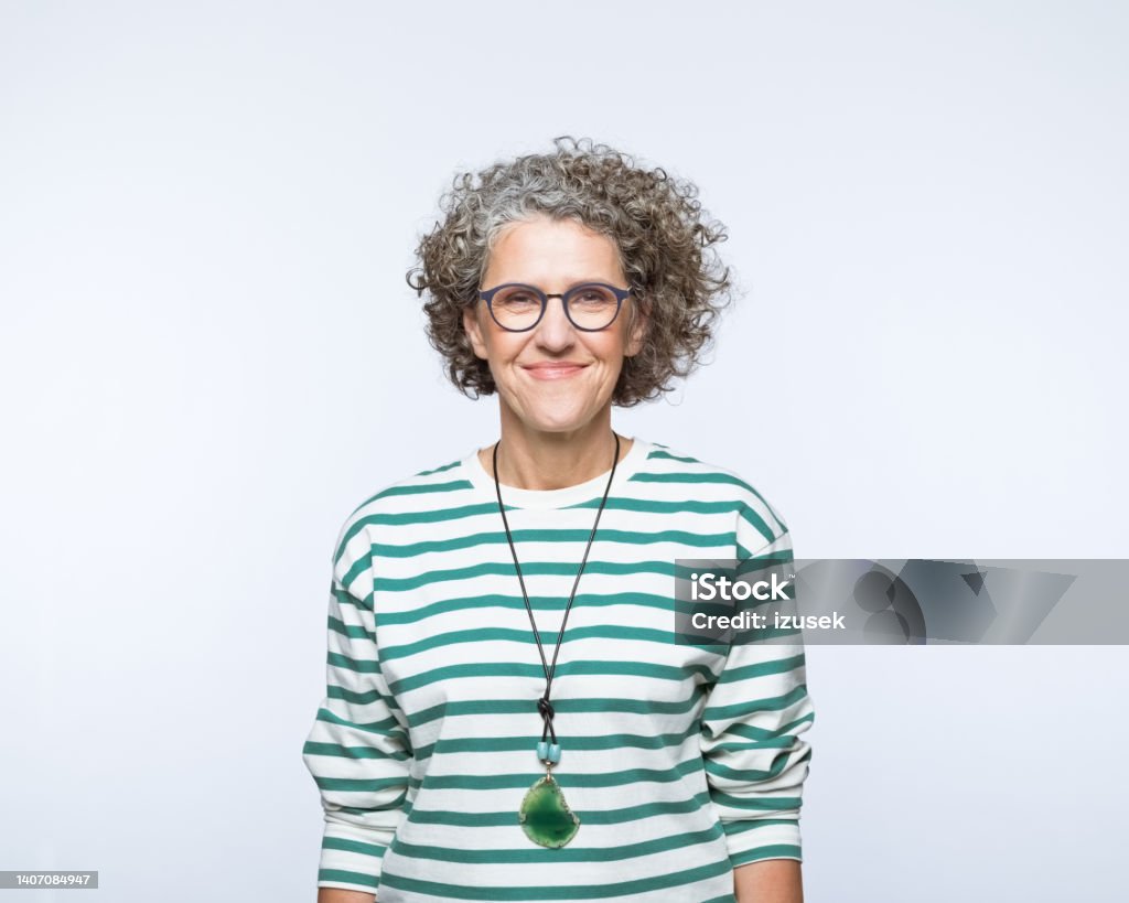 Portrait of smiling mature women Portrait of confident mature woman wearing striped blouse and eyeglasses, smiling at camera. Studio shot, grey background. Women Stock Photo