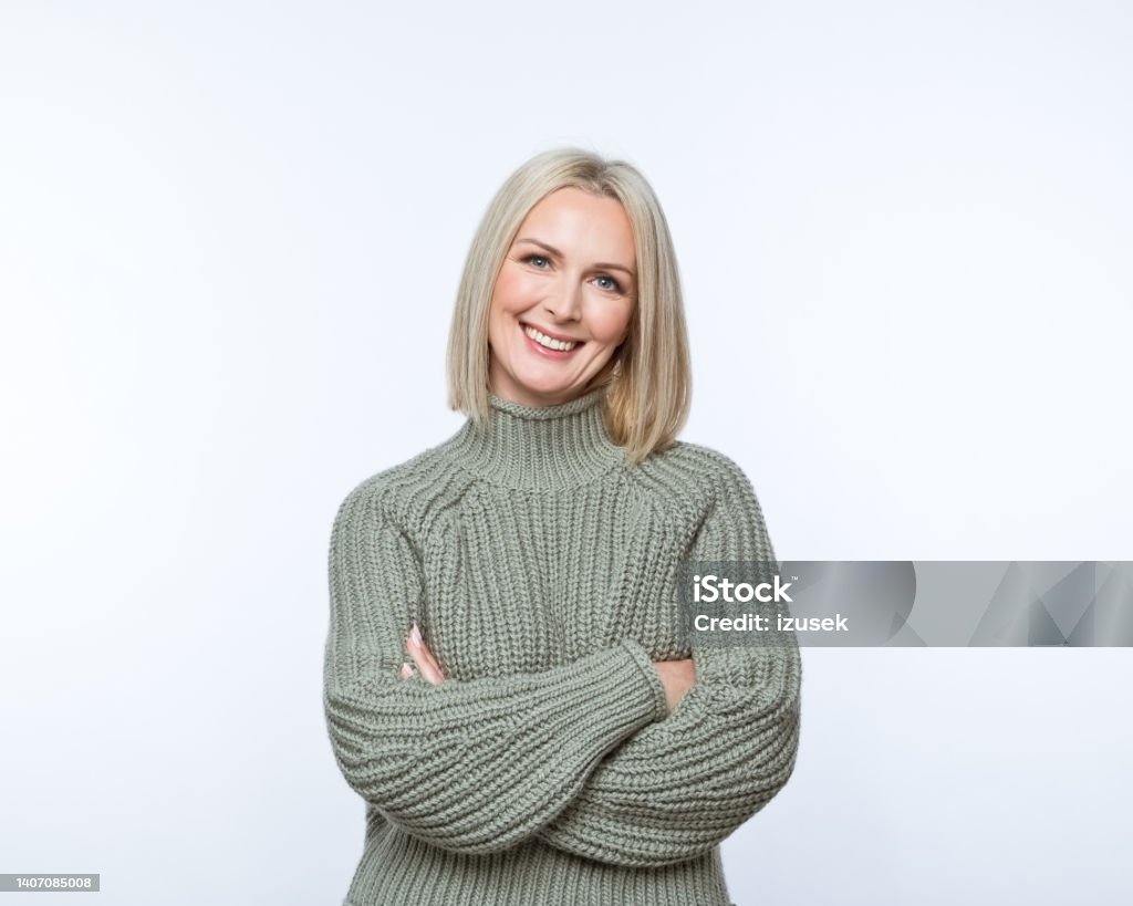 Portrait of smiling mature women Portrait of confident mature woman wearing khaki sweater, standing with arms crossed and smiling at camera. Studio shot, grey background. Women Stock Photo
