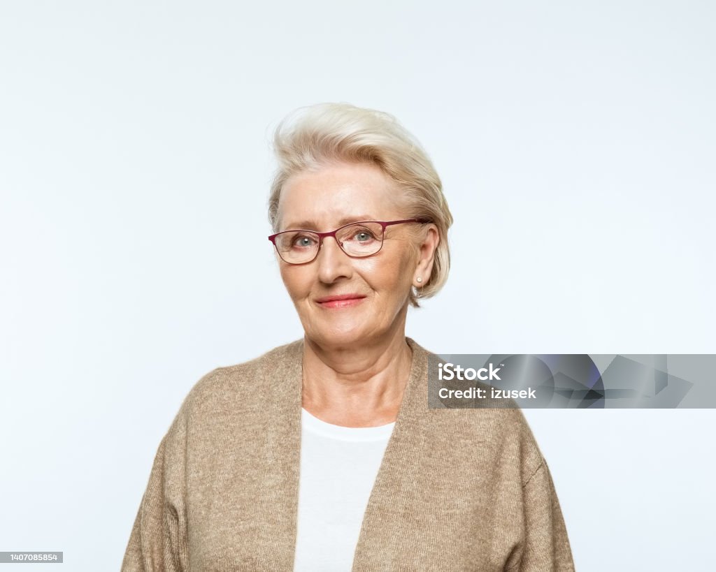 Portrait of smiling senior women Portrait of confident senior woman wearing beige cardigan, smiling at camera.. Studio shot, grey background. Portrait Stock Photo