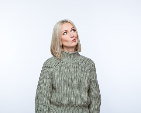 Portrait of cconfused mature woman wearing khaki sweater, looking away. Studio shot, grey background.