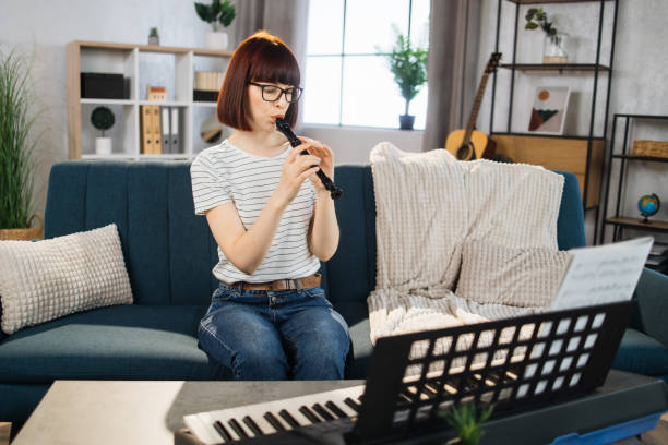 une jeune femme joue de la flûte dans un salon lumineux à la maison. - flute musical instrument music key photos et images de collection