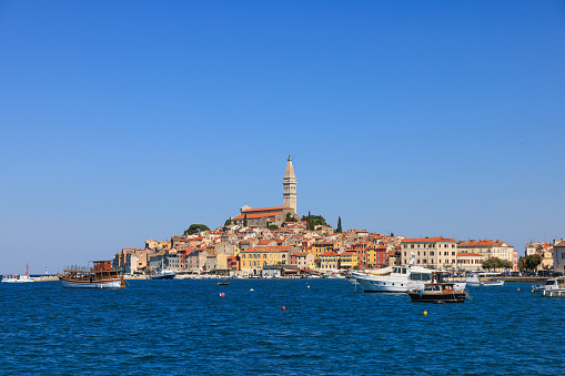 View on Rovinj old townscape with bell tower under the clear sky from remote location, blue sea with nautical vessels floating