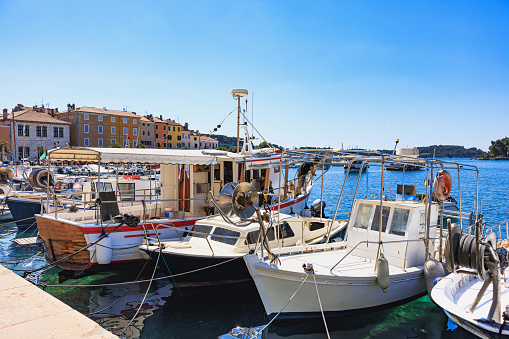 Boats anchored by the pier in Rovinj marina, townscape in the background under the clear sky