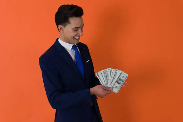 Photo of an elegant man dressed in formal blue suit holding a wad of bills while looking at it