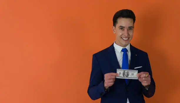 Photo of dapper man dressed in blue suit smiling while holding one US dollar