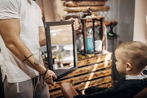 Barber showing haircut to a little boy too see it in the mirror in the barber shop