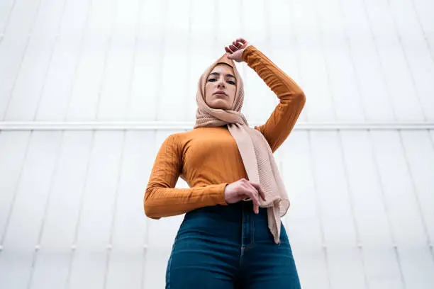 Beautiful young muslim woman wearing hijab standing against white background and looking at camera.