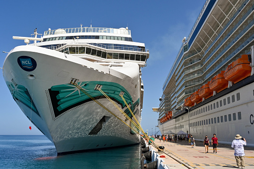 Kusadasi, Turkey - June May 2022: Passengers walking between two cruise ships in port. On the left is the Norwegian Jade cruise ship, which is operated by NCL.