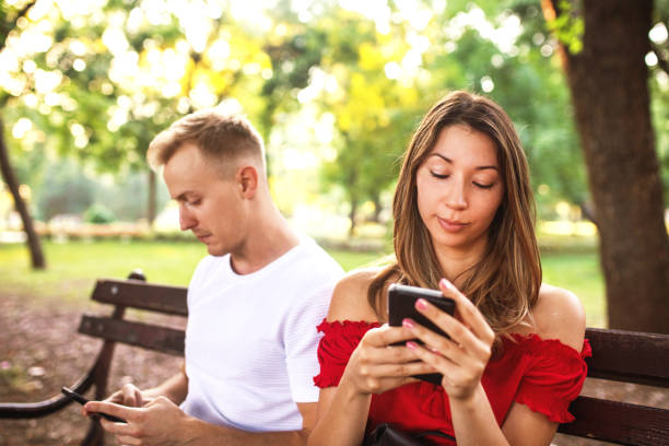 istock Young couple looking at their phones while in the park 1407092959