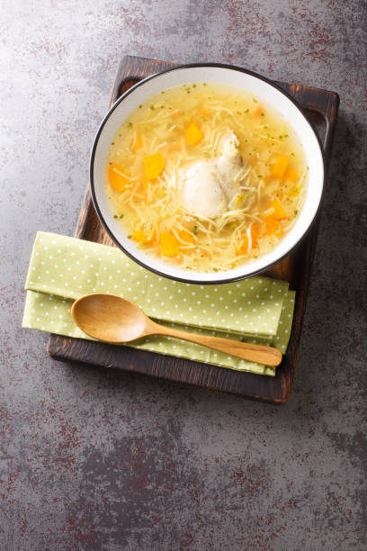 soupe de poulet légère avec des pâtes et des légumes en gros plan dans un bol sur un plateau en bois. vue verticale de dessus - carrot close up silverware cutting board photos et images de collection