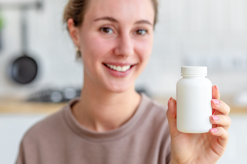Happy young woman holding bottle of dietary supplements or vitamins in her hands. Close up. Healthy lifestyle concept