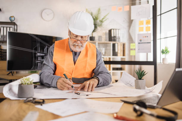 istock Senior builder, engineer in reflective vest uniform and hard hat on desk in office. 1407093411
