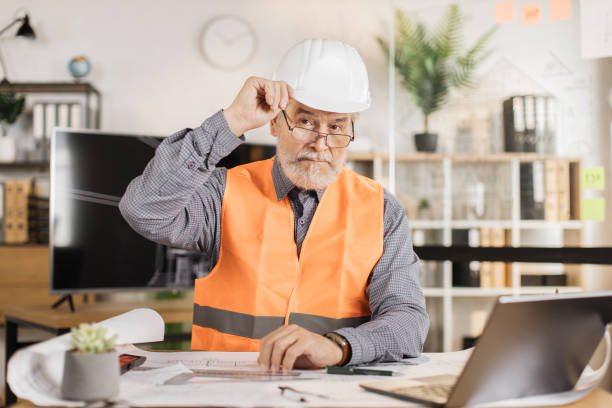 istock Professional senior male architect builder in white protective helmet and uniform using laptop 1407093431