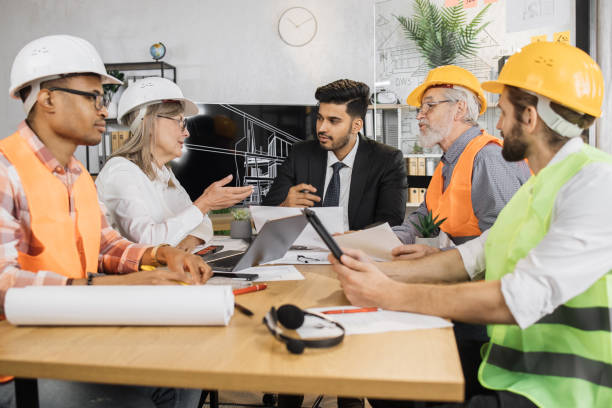 istock Five multiracial people architects sitting at desk in modern office and discussing common project 1407093439
