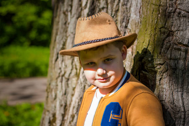 istock Cute boy posing in a cowboy hat in the woods by a tree. The sun's rays envelop the space. Interaction history for the book. Space for copying 1407095120