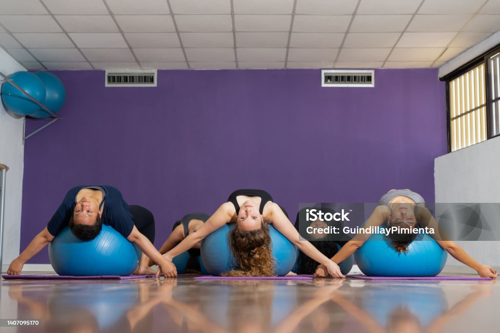 Group of women practicing pilates while doing exercise on a ball Group of women practicing pilates while doing exercise on a ball, purple background Gymnastics Stock Photo