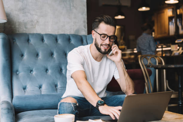 istock Positive man speaking on smartphone and using laptop in cafe 1407097803