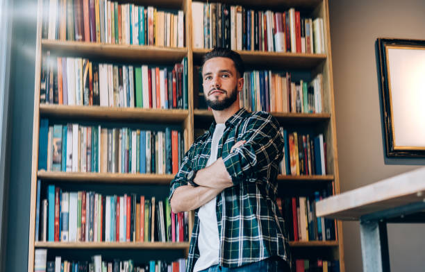 istock Smiling young bearded man looking away while standing in bookstore 1407097816