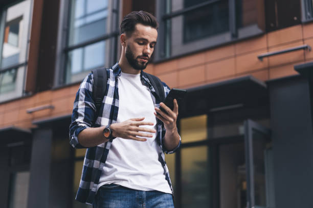 istock Focused young man using smartphone on city street 1407097840