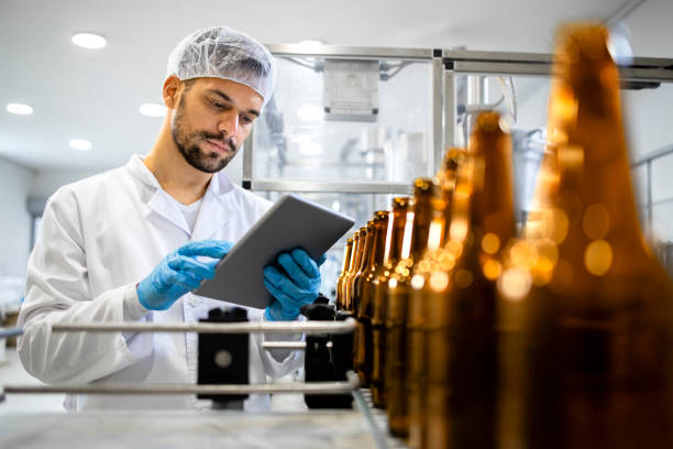 istock Bottled beer beverage production and factory worker controlling process on tablet computer. 1407098000