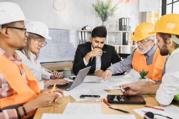 istock Architects and engineers in suits and helmets having working meeting at modern office. 1407098549