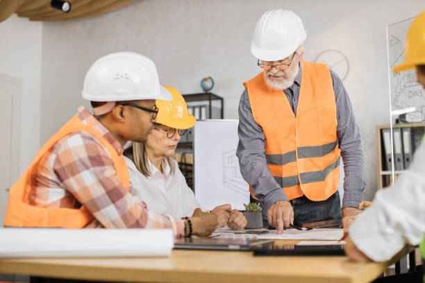 istock Multiracial architect people in helmets sitting at table with blueprints and modern devices. 1407098607