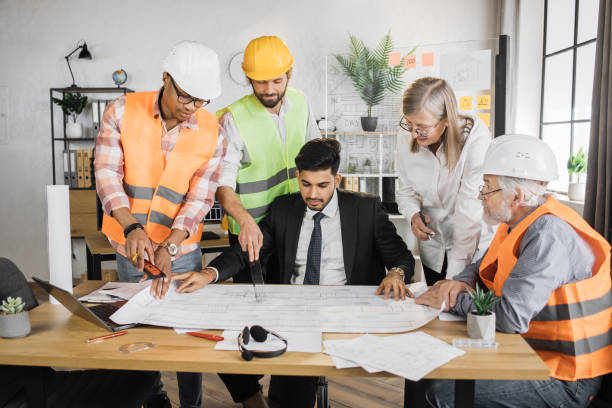istock Group of five multiracial people in suits and helmets brainstorming for common project of building. 1407098631