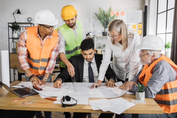 istock Group of five multiracial people in suits and helmets brainstorming for common project of building. 1407098632