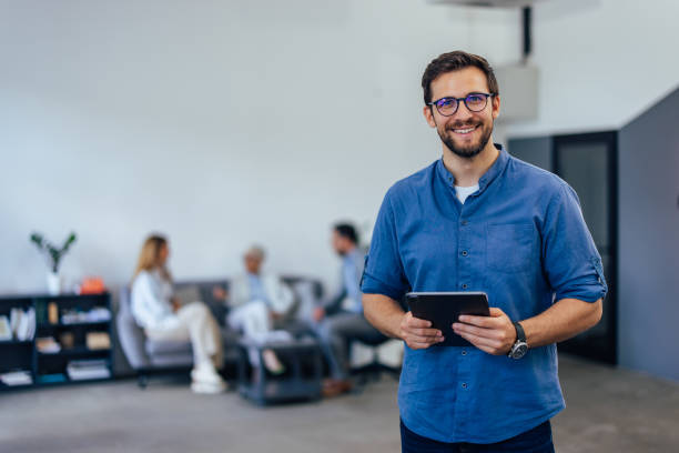 istock Elegantly dressed man, holding a tablet, smiling for the camera while being at the co-working space. 1407098872