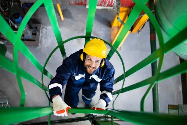 Refinery or industrial worker in safety equipment climbing up metal ladders or staircase. stock photo