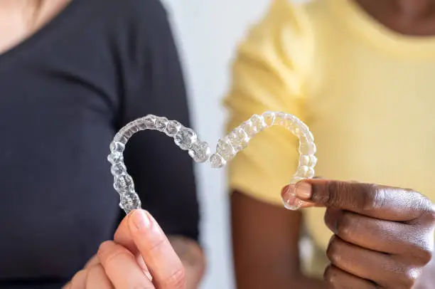 two interracial woman holind invisible dental aligners to form a heart shape