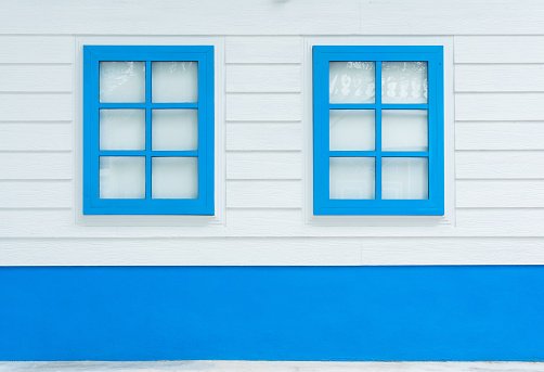 Two windows on white wood wall, outdoor view. Colorful blue window from front outside of house.