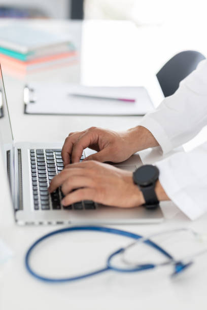 Close up of a doctors hands typing on laptop stock photo