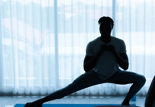 Young African man doing yoga exercise in the living room of his homewith the pleasure of relaxing with light sports In the morning atmosphere of the day.