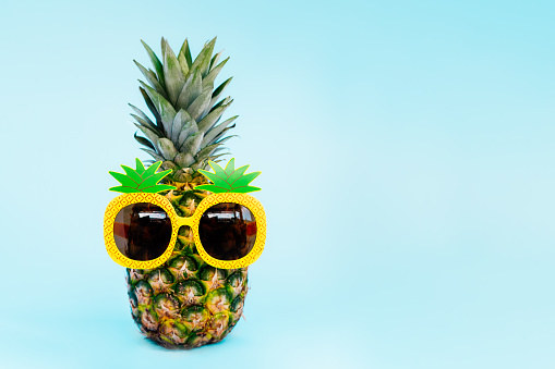 Funny pineapple in a sunglass of pineapple shape on the blue background. Tropical style summer on the beach vibes. Exotic fruits. Resort vacation creative concept. Selective focus. Copy space.