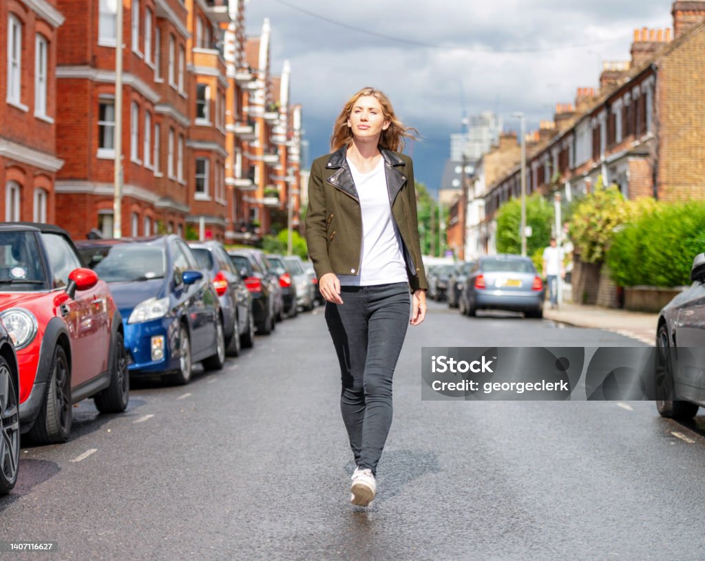 Portrait - middle of the street Full length portrait of a woman confidently walking towards the camera on a residential street in South London, UK. Walking Stock Photo