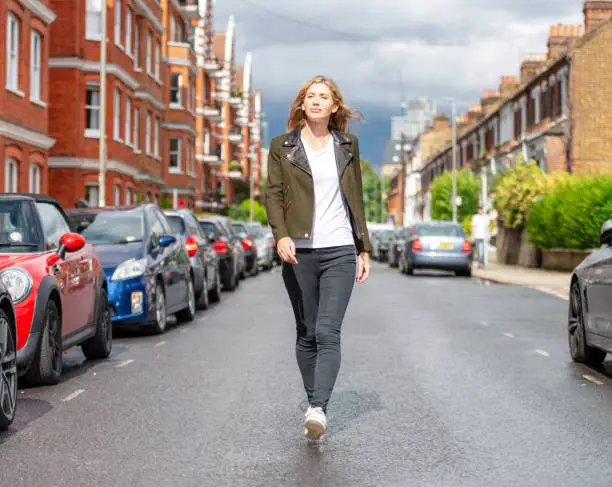 Full length portrait of a woman confidently walking towards the camera on a residential street in South London, UK.