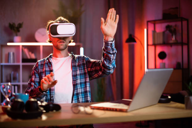 istock Young caucasian man sitting at home office and using VR glasses and laptop for remote work. 1407121416