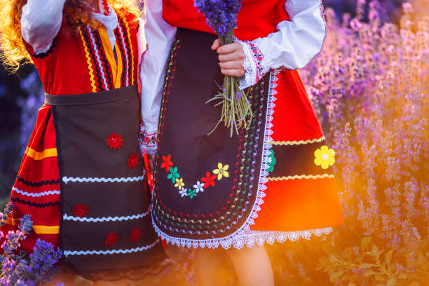 Beautiful girls in traditional Bulgarian folklore costumes in lavender field during harvest and sunset stock photo