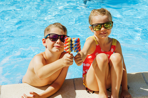 Happy siblings on vacation eating ice cream at swimming pool